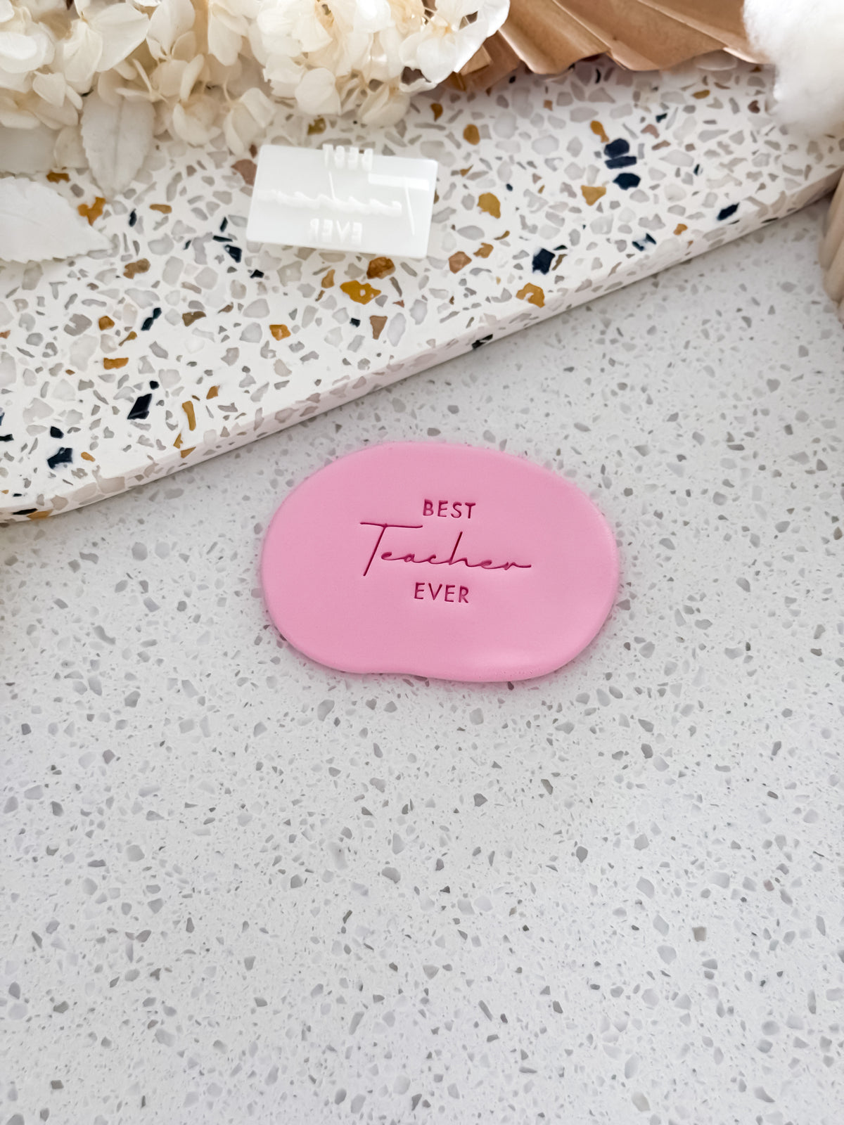 Best Teacher Ever cookie stamp by O'Khach, shown stamped in pink fondant